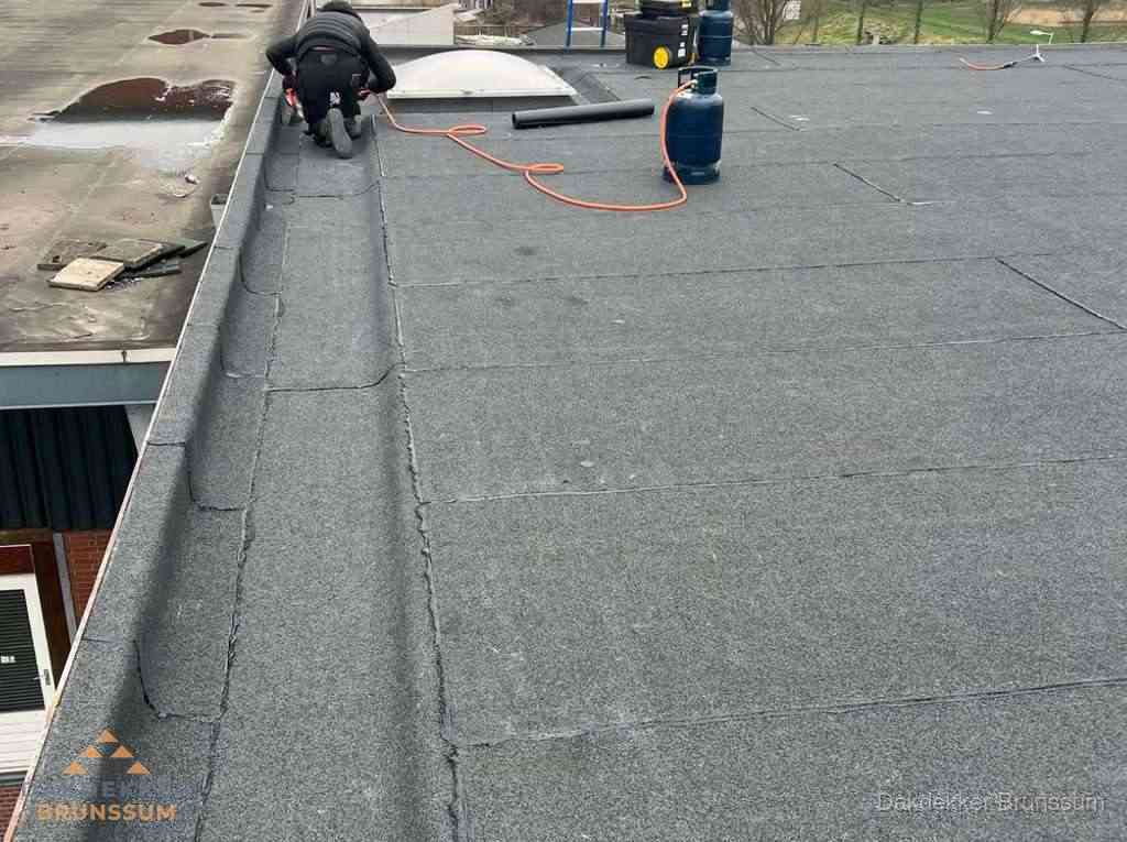 Dakdekker repareert bitumen dakbedekking op groot plat dak in Brunssum
